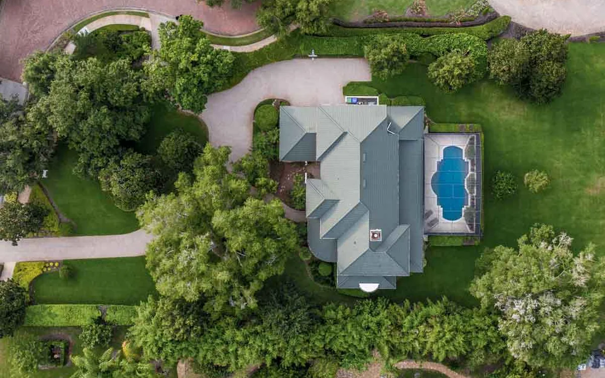 An aerial view of a large residential property with a pool and mature trees