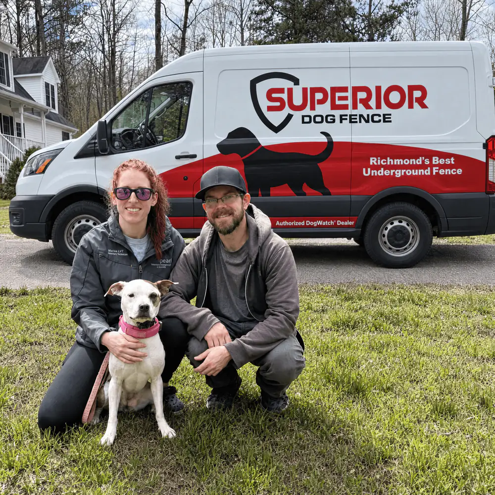 Two dog owners kneeling on a front lawn with their dog, the Superior Dog Fence van behind them