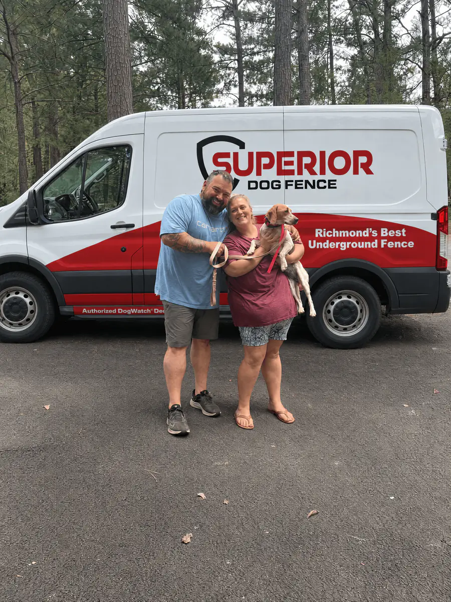 Two dog owners holding their small dog beside the Superior Dog Fence van outside their home.