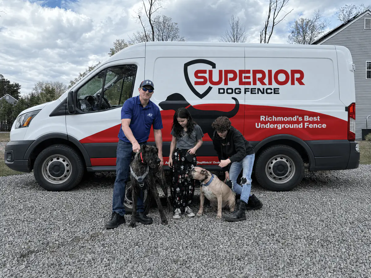 A family standing with their three dogs beside the Superior Dog Fence van