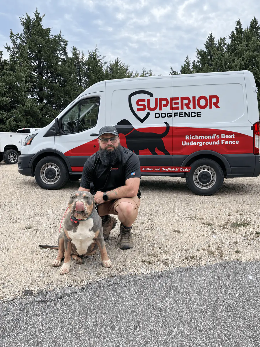 A Superior Dog Fence installer kneeling with a pit bull on a driveway beside the company van.