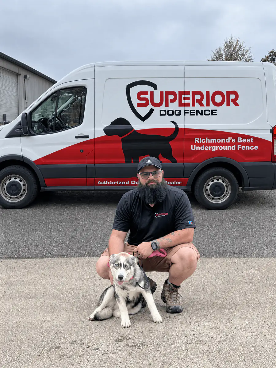 A Superior Dog Fence installer kneeling with an Australian shepherd puppy in front of the company van.