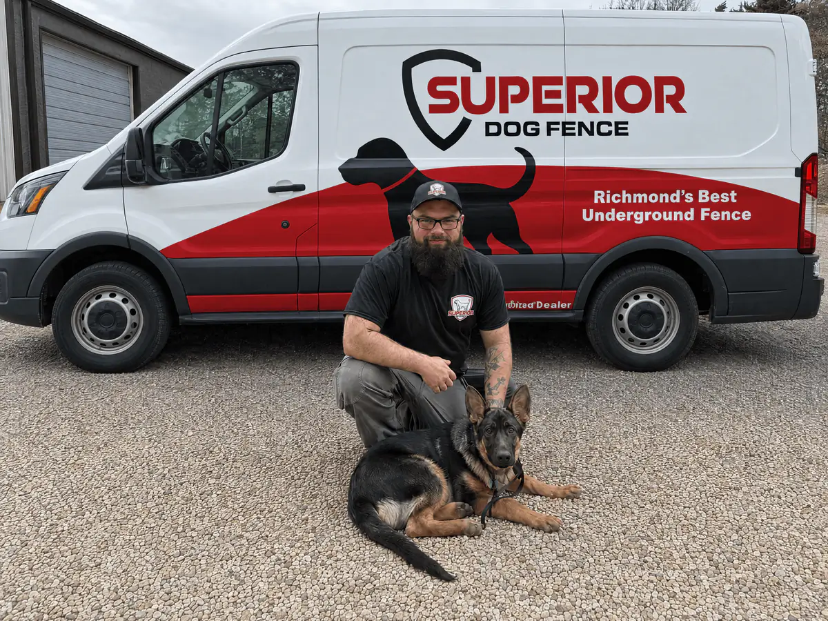 A Superior Dog Fence installer kneeling with a German shepherd in front of the company van.