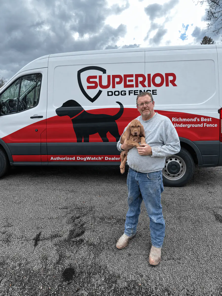 A dog owner holding an apricot doodle puppy in front of the Superior Dog Fence van.