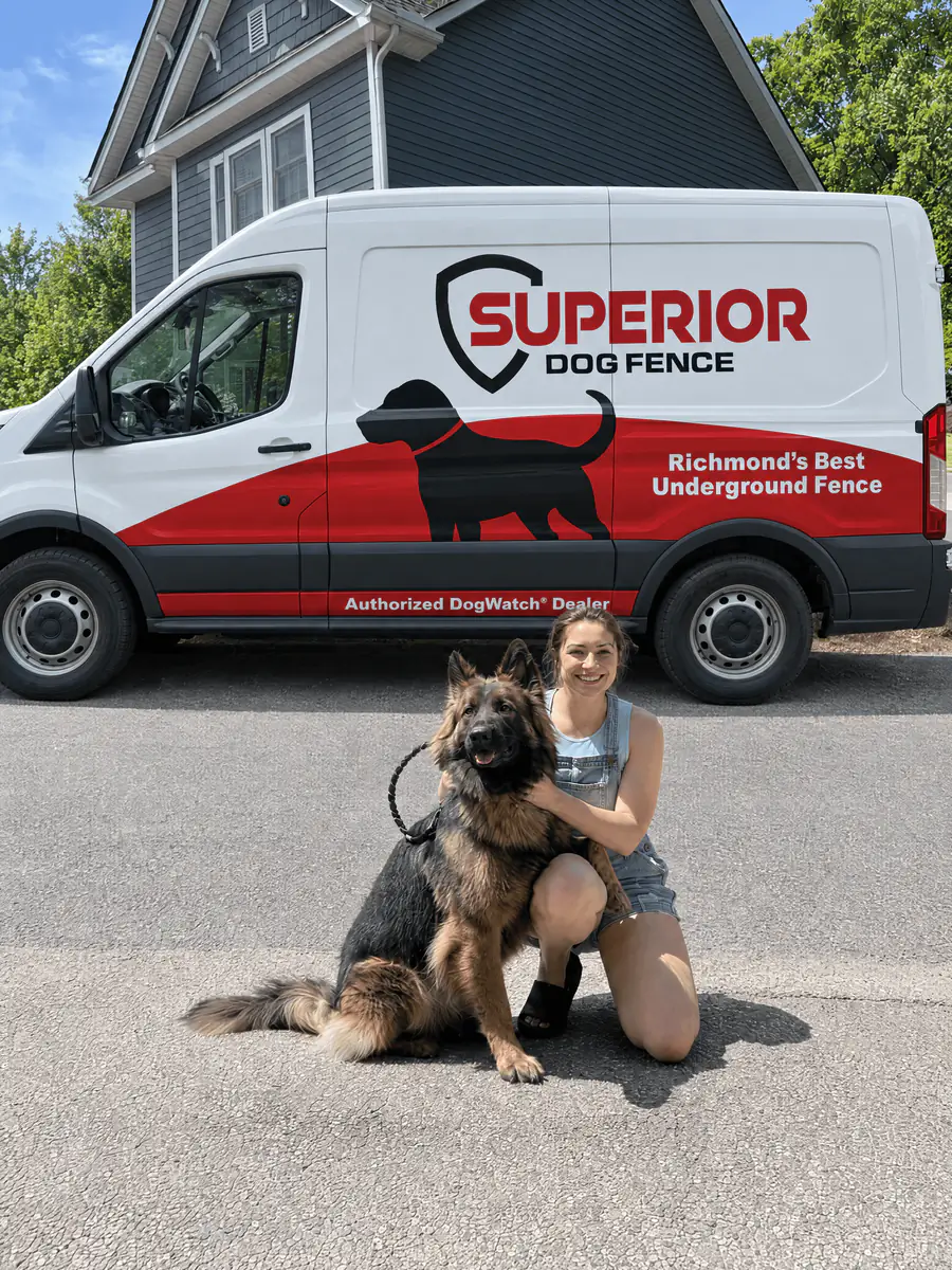 A dog owner kneeling beside a German shepherd in front of the Superior Dog Fence van.